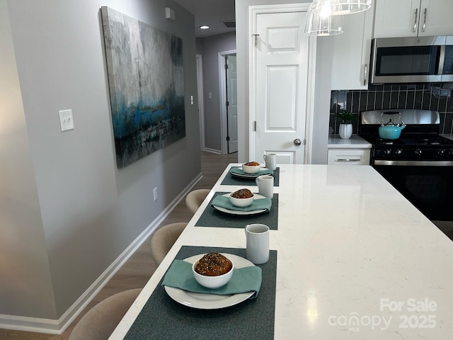 1004 Johnson St, Charlotte, NC 28206 - kitchen featuring stainless steel microwave, black range with gas cooktop, baseboards, tasteful backsplash, and white cabinets
