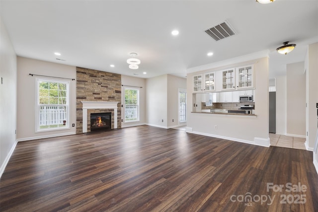 unfurnished living room featuring dark wood finished floors, plenty of natural light, a stone fireplace, baseboards, and recessed lighting