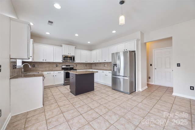 kitchen with stainless steel appliances, backsplash, a kitchen island, light tile patterned floors, and white cabinets