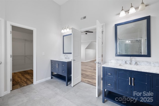 full bath featuring two vanities, a ceiling fan, a stall shower, a spacious closet, and baseboards