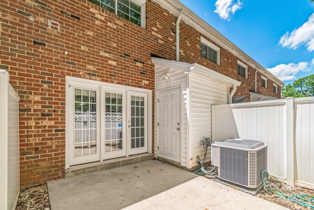 back of property featuring central AC, fence, brick siding, and a patio