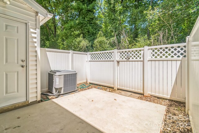 view of patio with central AC unit, a fenced backyard, and view of wooded area