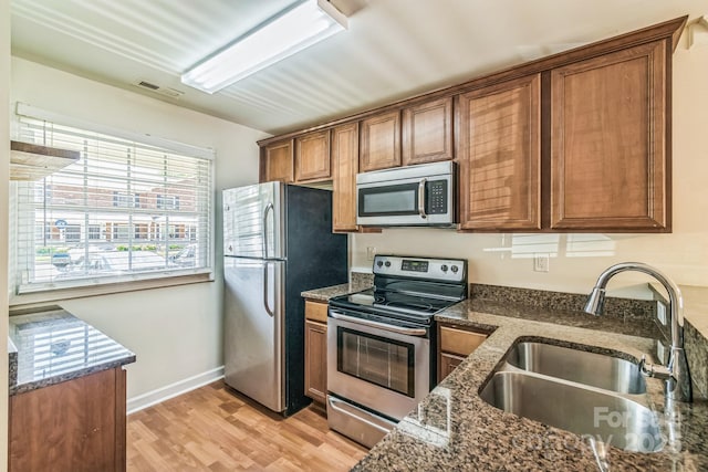 kitchen featuring appliances with stainless steel finishes, a sink, brown cabinets, and light wood-style flooring