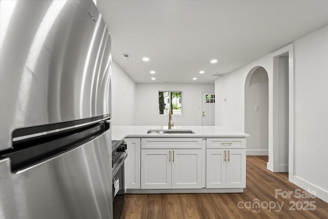 kitchen featuring freestanding refrigerator, a sink, a peninsula, dark wood-style flooring, and recessed lighting