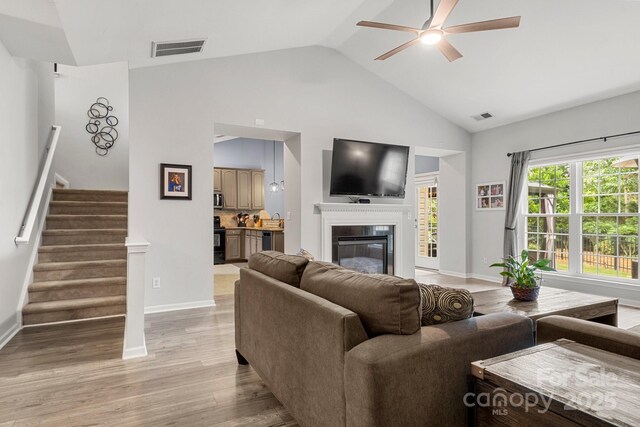3820 Leela Palace Way, Fort Mill, SC 29708 - living room featuring a ceiling fan, stairs, vaulted ceiling, light wood finished floors, and a glass covered fireplace