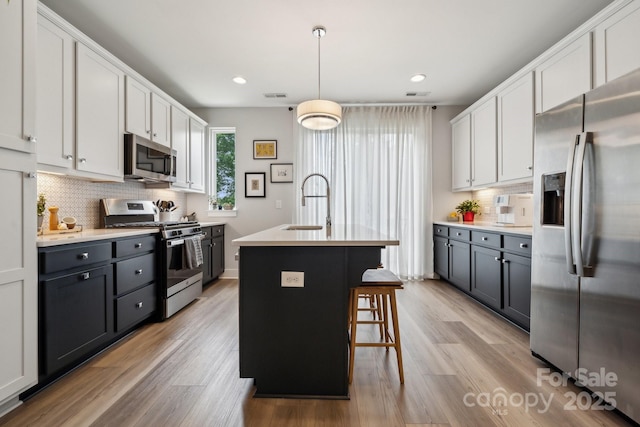 kitchen with appliances with stainless steel finishes, a sink, decorative backsplash, light countertops, and light wood-style floors