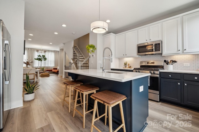 kitchen featuring appliances with stainless steel finishes, a sink, a breakfast bar area, tasteful backsplash, and light wood-style flooring