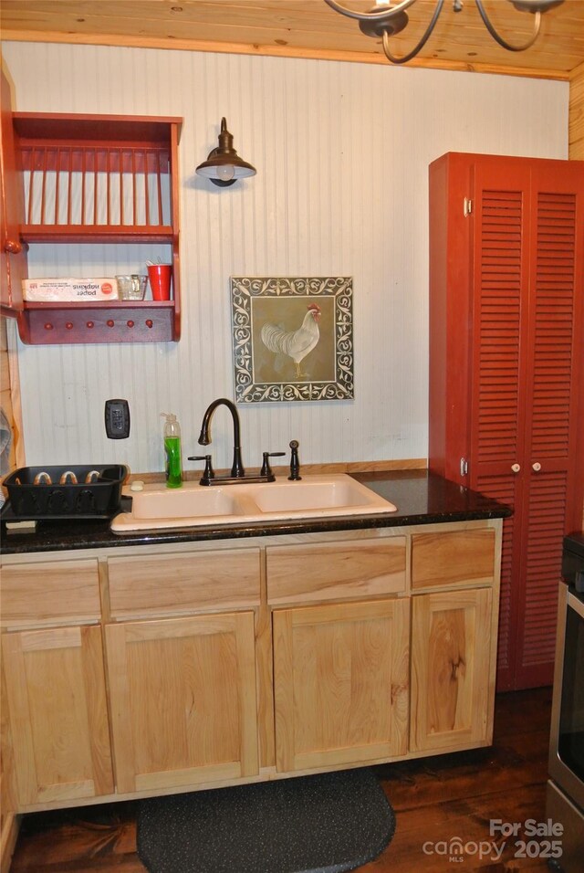 kitchen with a sink, light brown cabinetry, dark countertops, wood walls, and dark wood-style flooring