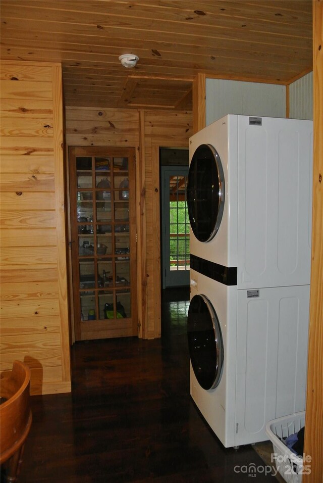 clothes washing area featuring wood ceiling, estacked washer and dryer, wood finished floors, and wooden walls