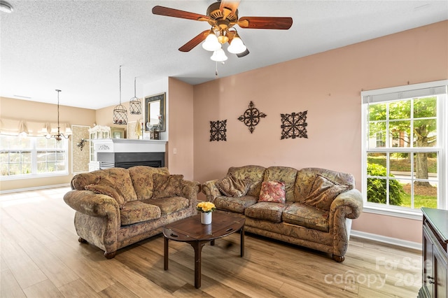 living area with light wood-style flooring, baseboards, a ceiling fan, a chandelier, and a fireplace