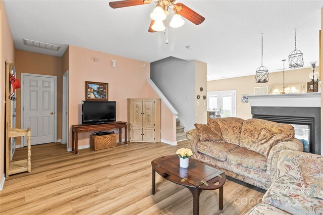 living room with light wood-style floors, ceiling fan, stairs, baseboards, and a multi sided fireplace