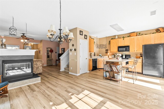 kitchen with black appliances, a multi sided fireplace, light countertops, light wood-type flooring, and a kitchen island