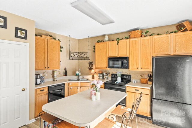 kitchen with black appliances, a sink, light countertops, a center island, and light brown cabinetry