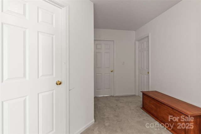 corridor featuring light colored carpet and baseboards