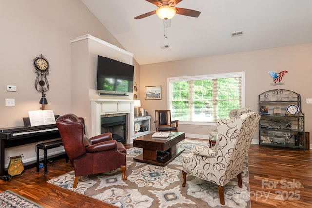 living area with wood finished floors, a tiled fireplace, a ceiling fan, high vaulted ceiling, and baseboards