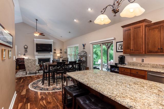 kitchen featuring dark wood finished floors, lofted ceiling, brown cabinetry, light stone countertops, and a ceiling fan