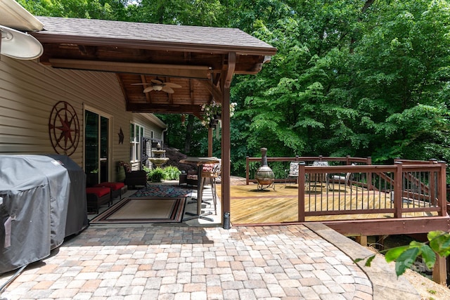 view of patio with ceiling fan, a wooden deck, and view of wooded area