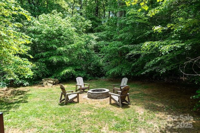 view of green lawn featuring an outdoor fire pit and a forest view