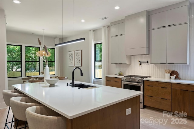 kitchen featuring stainless steel range with gas cooktop, a sink, modern cabinets, light wood-style flooring, and brown cabinets