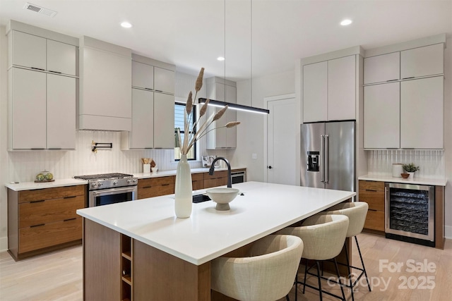 kitchen featuring wine cooler, tasteful backsplash, light wood-type flooring, premium appliances, and recessed lighting