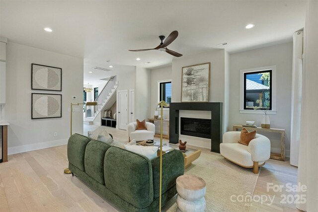 living area featuring light wood-style flooring, stairs, a glass covered fireplace, healthy amount of natural light, and recessed lighting