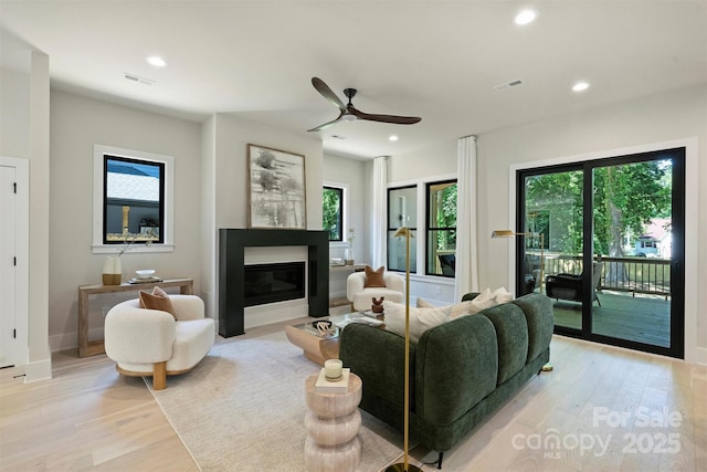living room with a glass covered fireplace, light wood-type flooring, plenty of natural light, recessed lighting, and a ceiling fan