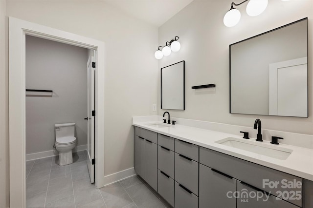 bathroom featuring baseboards, double vanity, toilet, and tile patterned flooring