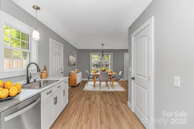 kitchen featuring dishwasher, a sink, light wood-style floors, white cabinets, and light countertops