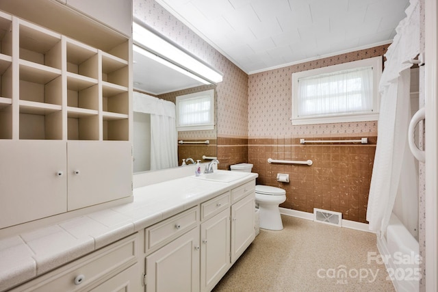 bathroom with wallpapered walls, toilet, vanity, curtained shower, and a wainscoted wall