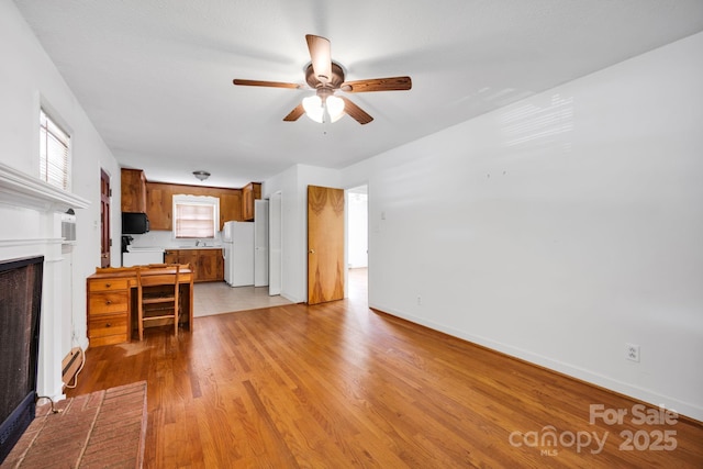 unfurnished living room featuring a fireplace, a ceiling fan, a sink, baseboards, and light wood-style floors