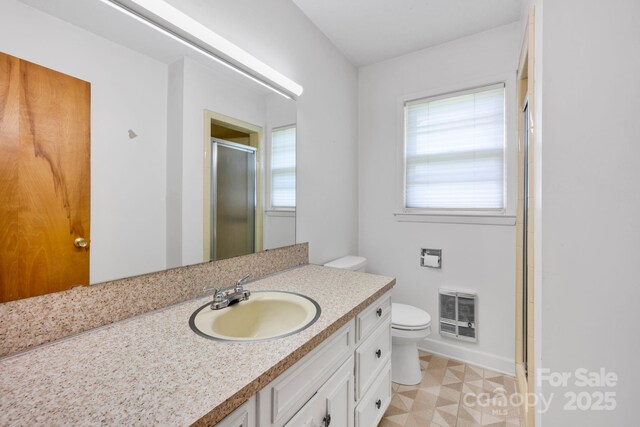 bathroom featuring a stall shower, toilet, vanity, heating unit, and tile patterned floors