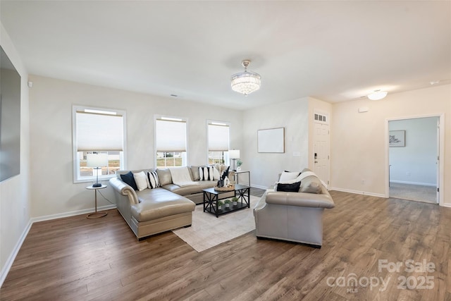 living area with baseboards, wood finished floors, and a chandelier