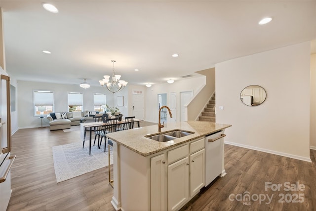 kitchen with a sink, dishwasher, wood finished floors, light stone counters, and decorative light fixtures