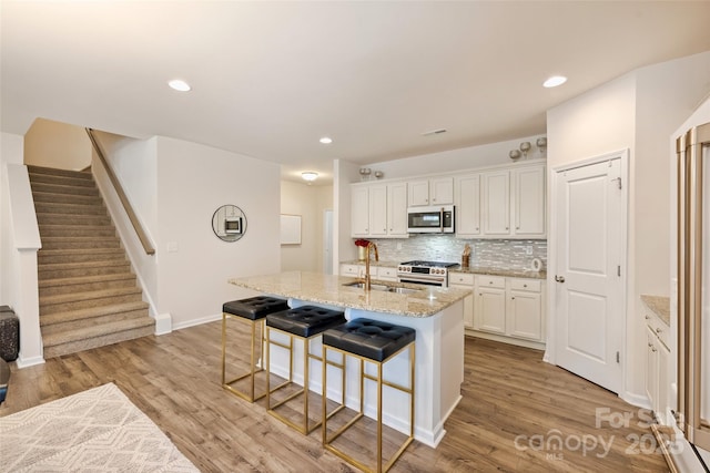 kitchen with a sink, stainless steel appliances, a breakfast bar area, white cabinets, and an island with sink