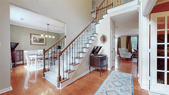 stairs with wood finished floors, a chandelier, crown molding, and baseboards