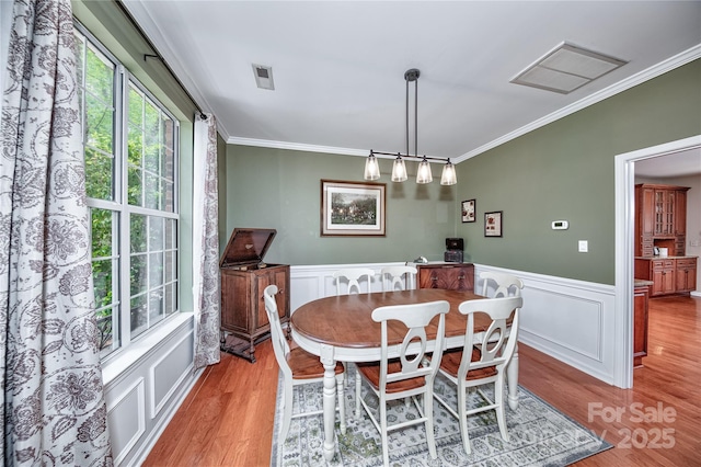 dining space with ornamental molding, wood finished floors, a wainscoted wall, and a decorative wall