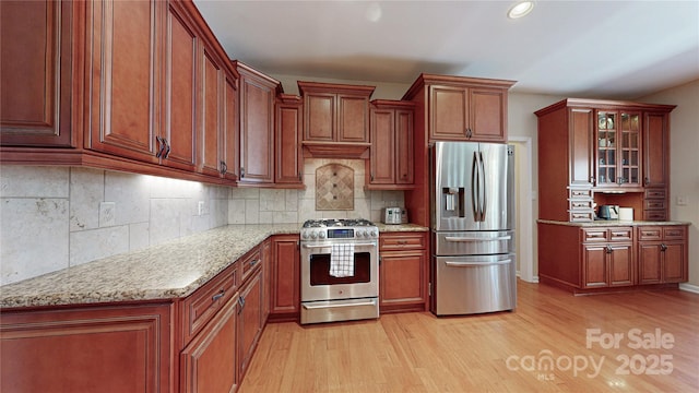 kitchen with appliances with stainless steel finishes, light wood-type flooring, glass insert cabinets, tasteful backsplash, and recessed lighting