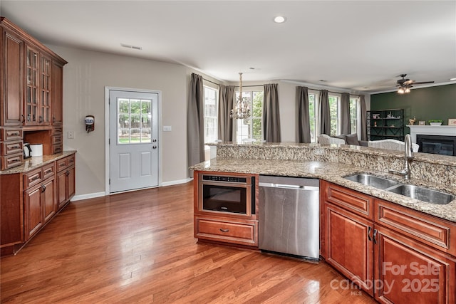 kitchen with stainless steel appliances, a sink, light wood finished floors, ceiling fan, and a glass covered fireplace