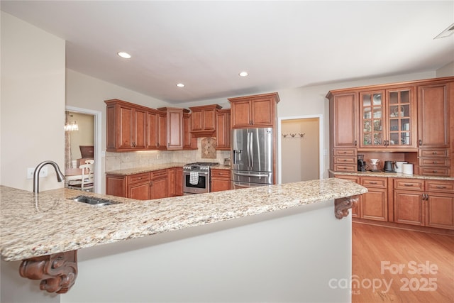 kitchen with stainless steel appliances, a sink, light wood-style floors, decorative backsplash, and brown cabinetry