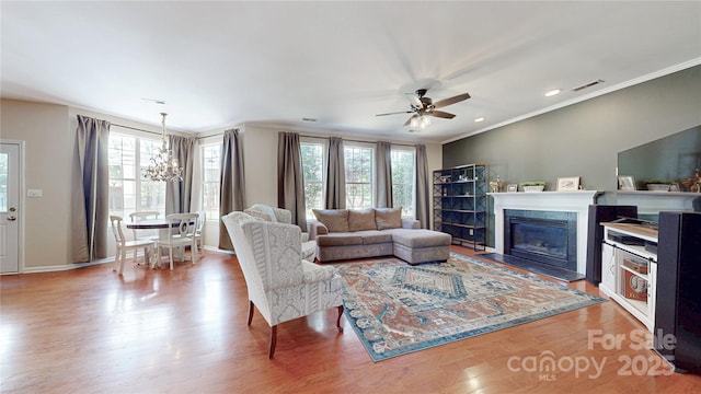 living area with a chandelier, a glass covered fireplace, wood finished floors, ceiling fan, and baseboards
