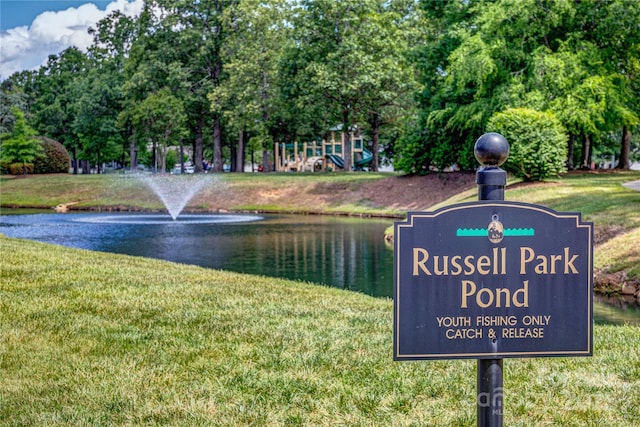 view of home's community with a water view, a lawn, and view of wooded area