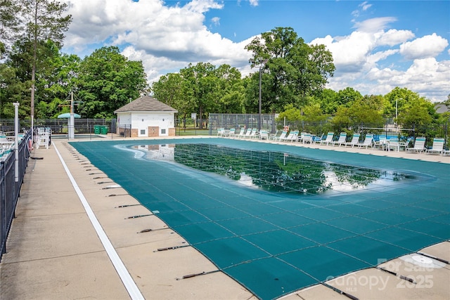 community pool with fence, view of wooded area, and a patio area
