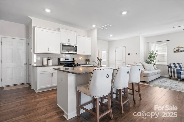 kitchen with appliances with stainless steel finishes, a center island with sink, a kitchen breakfast bar, dark wood finished floors, and decorative backsplash