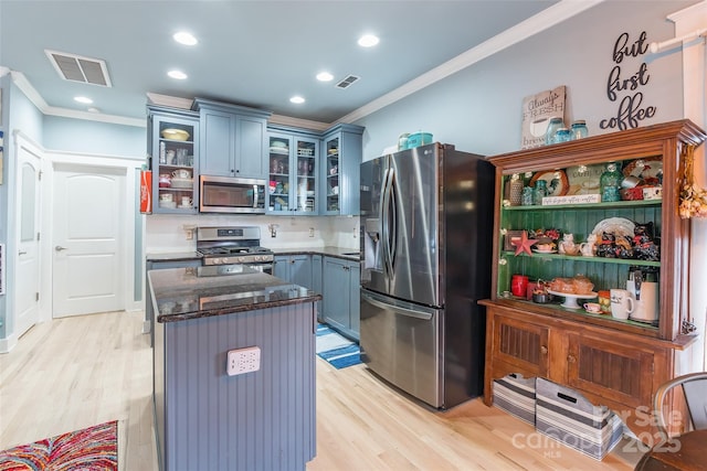 kitchen with appliances with stainless steel finishes, crown molding, blue cabinetry, light wood-style flooring, and a kitchen island