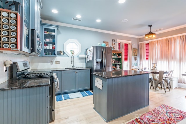 kitchen featuring a sink, stainless steel appliances, crown molding, a kitchen island, and dark stone countertops