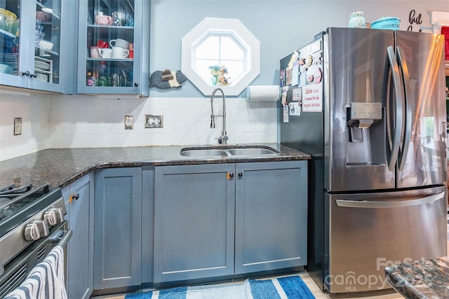 kitchen featuring stainless steel appliances, a sink, backsplash, and dark stone counters
