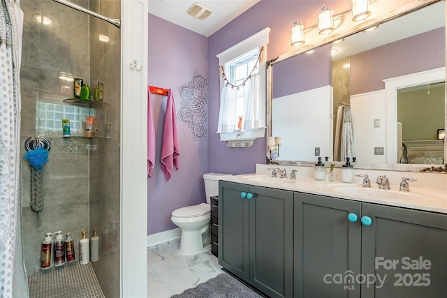 bathroom with a tile shower, marble finish floors, toilet, double vanity, and baseboards