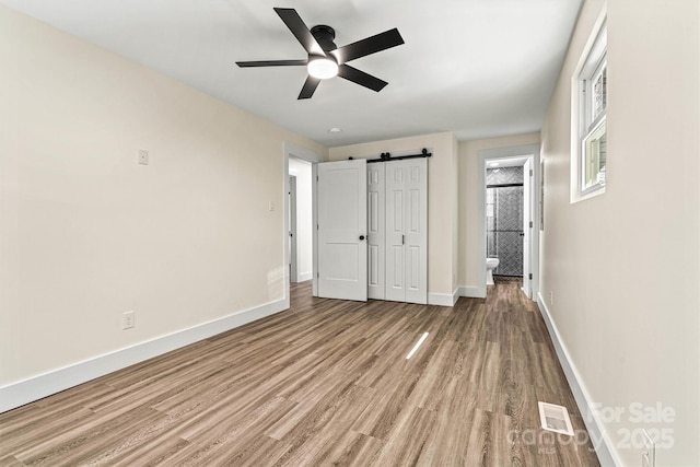139 Elysian Dr, Mooresville, NC 28117 - unfurnished bedroom with light wood-style floors, baseboards, a barn door, ensuite bathroom, and ceiling fan
