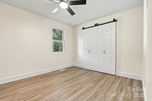139 Elysian Dr, Mooresville, NC 28117 - unfurnished bedroom with light wood finished floors, a barn door, baseboards, a closet, and a ceiling fan