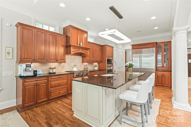 6831 Conservatory Ln, Charlotte, NC 28210 - kitchen featuring decorative columns, built in appliances, a sink, brown cabinets, and light wood-type flooring